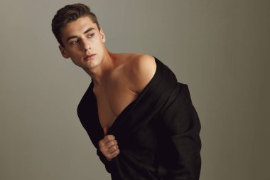 Bej arka planda siyah ceketli çekici bir adam portresi.