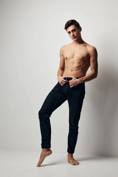 Ein gutaussehender junger Mann in Hose steht auf einem Bein und hält seine Hände am Gürtel — Stockfoto