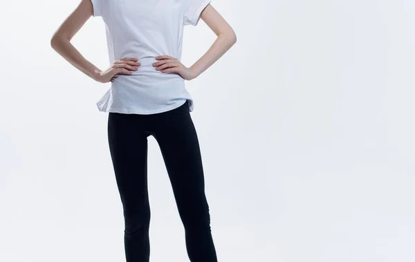 Спортсменка в білій футболці і легінсах на світлому фоні розтягує ноги по боках — стокове фото