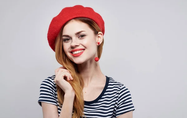 Mujer alegre con sombrero rojo y camiseta a rayas haciendo gestos con las manos y sonriendo —  Fotos de Stock
