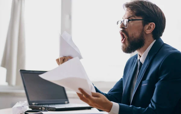 Impulsive man with white sheets of paper in hands emotions office business finance laptop