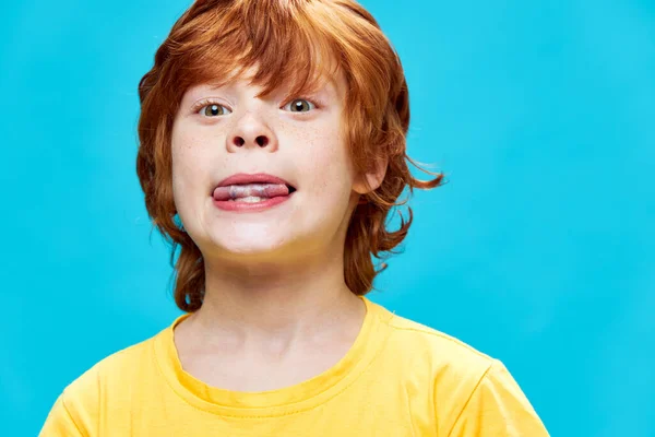 Ginger child close-up bites his tongue yellow t-shirt — Stock Photo, Image