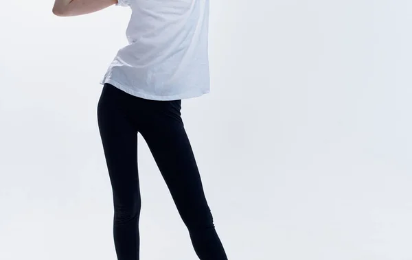 Egy atlétikus nő fehér pólóban és könnyű hátterű lábszárvéddel oldalt széttárta a lábait. — Stock Fotó