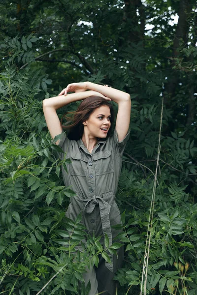 Mujer en el bosque sostiene sus manos detrás de su cabeza y mira hacia otro lado así la naturaleza viaja —  Fotos de Stock