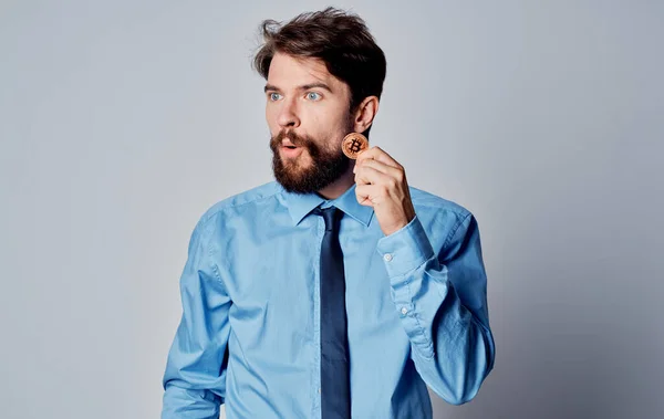 Hombre de negocios en una camisa azul con una moneda en sus manos Bitcoin fondo gris — Foto de Stock