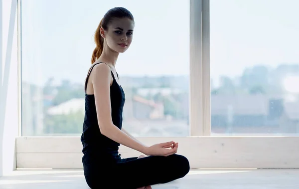 Жінка і ноги схрещені сидить на підлозі в приміщенні біля вікна і робить йогу — стокове фото