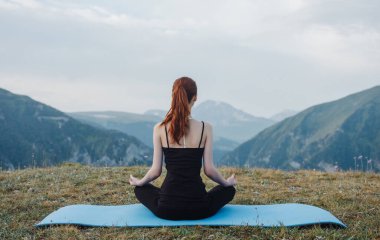 Doğada sportif bir kadın, dağların arka planında yoga yapıyor.