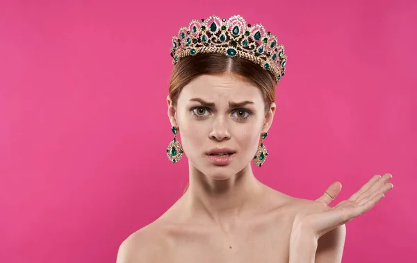 Emotional woman with a crown on her head on a pink background princess model