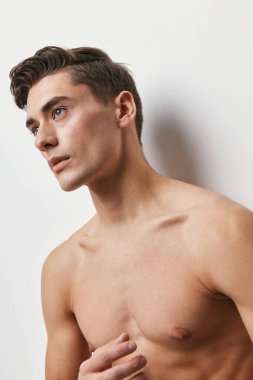 Çıplak gövdeli bir adam açık bir arkaplanda ileriye bakıyor.