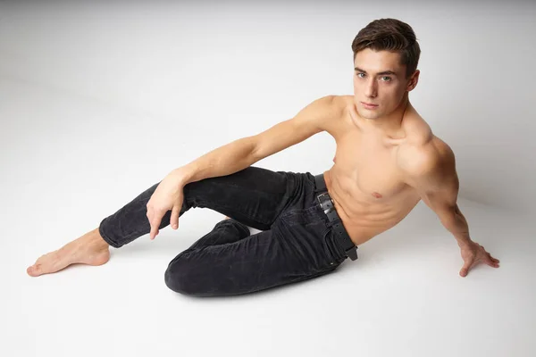 Молодий хлопець з голим торсом сидить на підлозі ізольований фон сучасного стилю — стокове фото