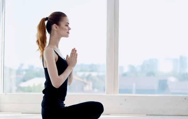 Mujer practica yoga mientras está sentada en el suelo dentro de la ventana en pleno crecimiento — Foto de Stock
