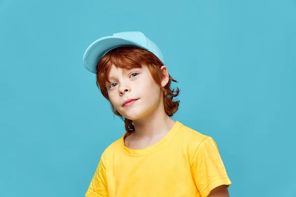 青い帽子の赤い髪の男の子の肖像画黄色のTシャツスタジオ — ストック写真