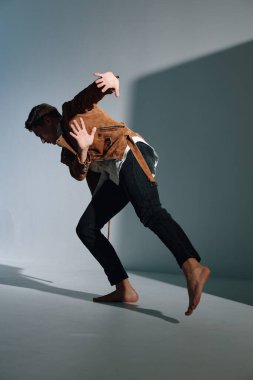 Kahverengi ceketli adam elleriyle hareket ediyor ve düz zemine tırmanıyor.