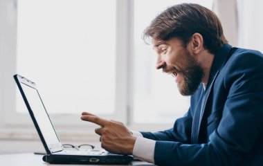 Masada takım elbiseli bir iş adamı ve pencerenin yanında bir dizüstü bilgisayar.