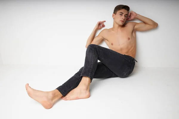 Carino giovane ragazzo con un torso nudo si siede sul pavimento a piedi nudi sfondo isolato — Foto Stock