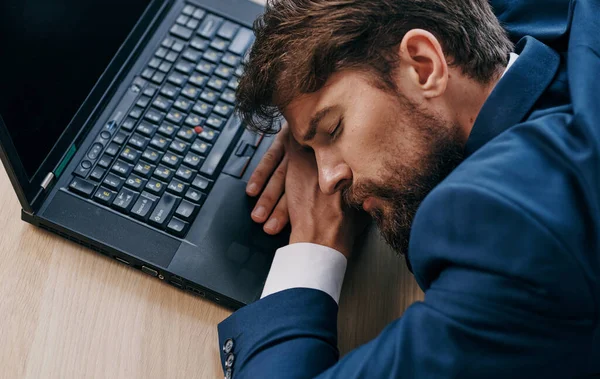 Homem em um terno em uma mesa de trabalho na frente de um escritório de laptop cansado — Fotografia de Stock