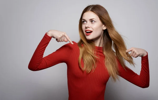 Mulher emocional gesticulando com as mãos em um fundo leve vermelho suéter modelo maquiagem — Fotografia de Stock