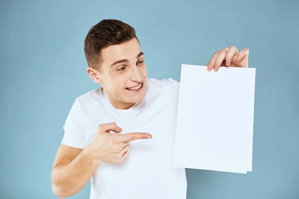 Man holding a sheet of paper in his hands white t-shirt cropped view blue background — Stock Photo, Image