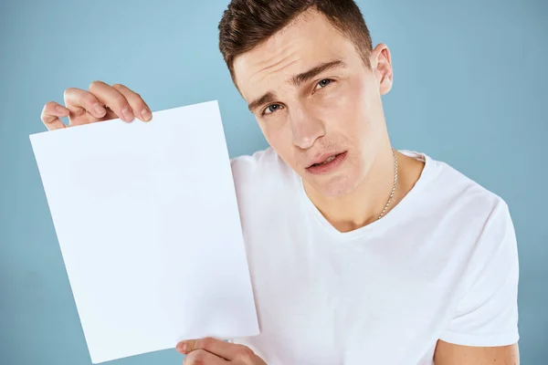 Een man in een wit t-shirt heeft een vel papier kopieerruimte — Stockfoto