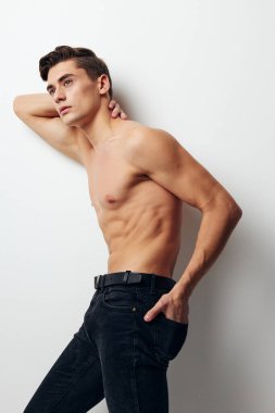 Çıplak gövdeli ve koyu renk pantolonlu bir adam elini açık arkaplanda tutuyor.