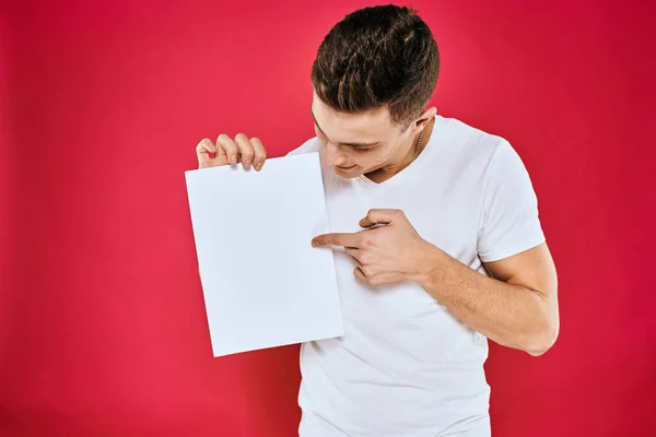 Emotionele man met een vel papier kopieerruimte t-shirt rode achtergrond — Stockfoto