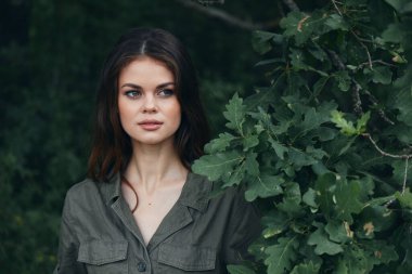 Ormandaki kadın yeşil çalıların yanında duruyor ve temiz havaya bakıyor. 