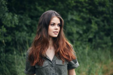 Ormandaki kadın uzun saçlı, yeşil takım elbiseli temiz havaya bakıyor. 