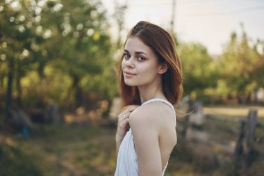 Arka planda yaz tatilinde bahçede ve ağaçlarda kızıl saçlı bir kadının portresi.