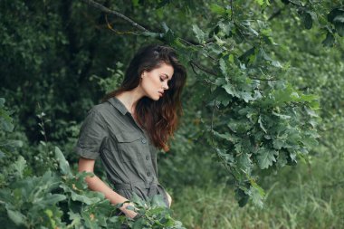 Ormandaki kadın aşağı bakar ve ellerini cebinde tutar. 