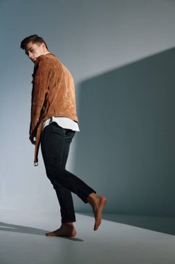 Kahverengi ceketli yakışıklı bir adam gri arka planda yürür.