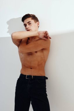 Çıplak gövdeli bir adam kollarını açık arkaplanda kendine sarılıyor ve siyah pantolon kesilmiş bir manzara.