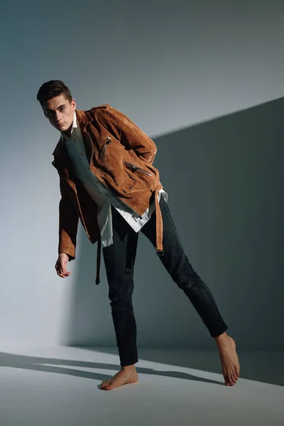 Хлопець в коричневій куртці на сірому фоні, схиленому до сторони, і джинси є моделлю — стокове фото
