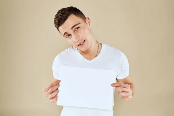 Man in wit t-shirt vel papier in handen kopiëren ruimte bijgesneden weergave beige achtergrond — Stockfoto