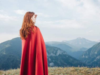 Bir kadın doğadaki dağlara ve omuzlarında kırmızı bir ekoseye bakar.