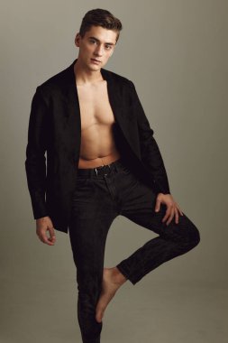 Siyah gömlekli yakışıklı bacağı bükülmüş, manken pozu veren çekici bir adam.