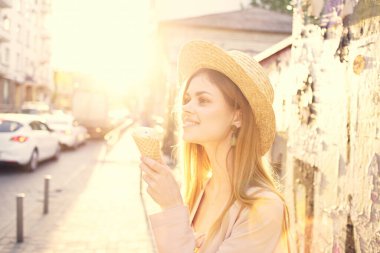 Şapkalı neşeli bir kadın dondurma yiyor açık havada güneşleniyor.