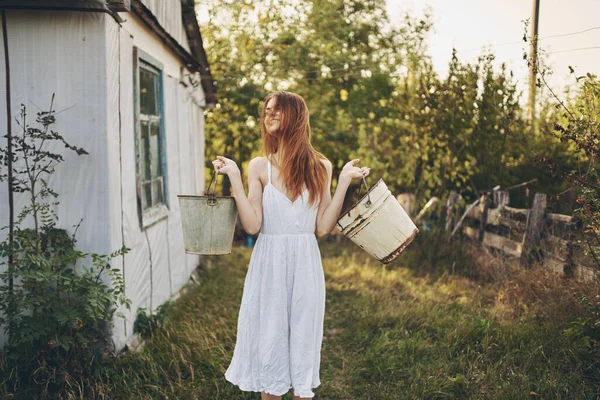 Comment était-ce une femme heureuse avec des seaux près d'un bâtiment dans un village de ferme nature — Photo