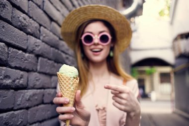 Güneş gözlüklü neşeli kadın ellerinde dondurmayla dışarıda siyah tuğlalı Wall Street tarzı