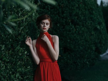 Kırmızı elbiseli güzel kadın çalılıkların yanında lüks bir cazibe