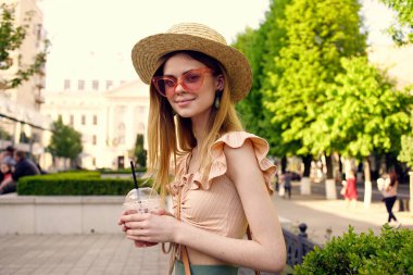 Şapkalı ve gözlüklü güzel bir kadın sokakta parkta yürüyor.