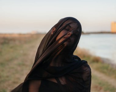 Kafasında siyah kumaşlı bir kadın nehrin kenarında.