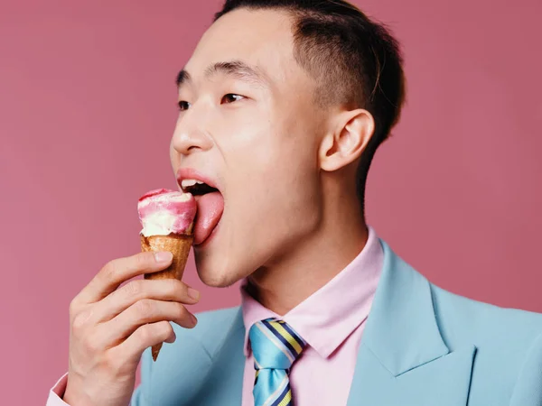 幸せなアジアの男はピンクの背景にアイスクリームを舐め — ストック写真