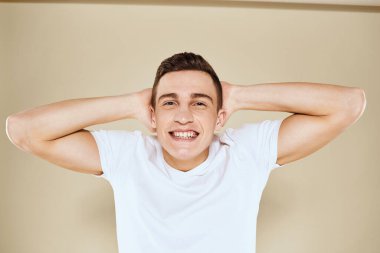 Duygusal erkek yüz ifadesi jesti elleri beyaz tişört bej arka planı