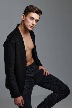 Gri arka planda bacağını kaldırmış takım elbiseli yakışıklı bir adam.