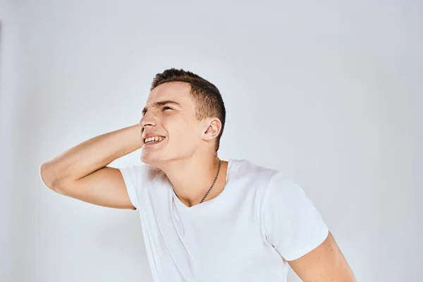 El hombre emocional con una camiseta blanca sostiene su mano sobre su rostro fondo claro —  Fotos de Stock