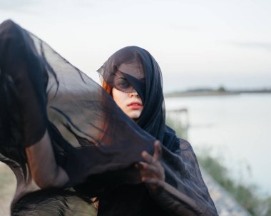 Doğada elinde siyah bir bez olan kızıl saçlı bir kadın.