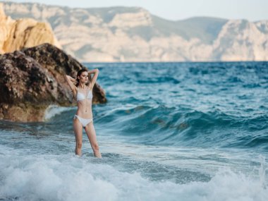 Plajda mayo giymiş güzel bir kadın ve okyanus kayalarının berrak suları turizmi gezer.
