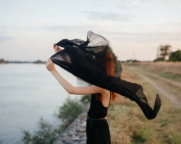 Uma mulher em um vestido com um lenço preto ao ar livre perto do rio — Fotografia de Stock