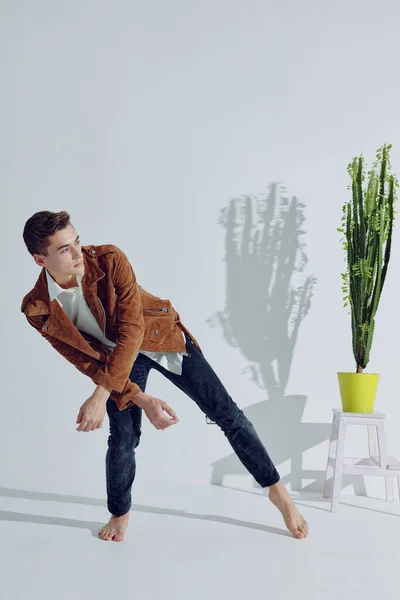 Um cara elegante está gesticulando com as mãos em um quarto brilhante e inclinado para o lado perto de uma flor em um pote — Fotografia de Stock