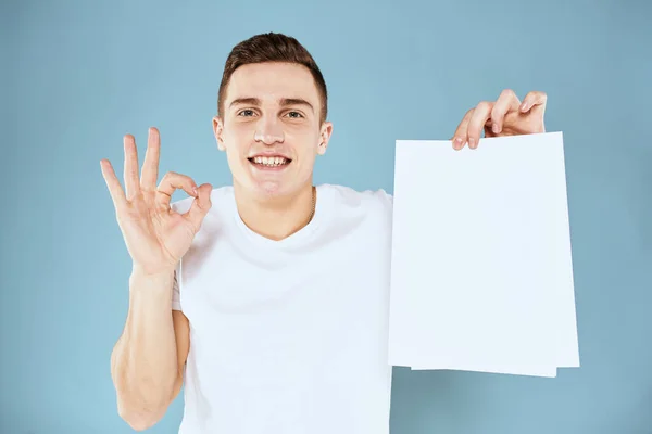 Mężczyzna trzyma kartkę papieru w jego rękach biały t-shirt przycięty widok niebieski tło — Zdjęcie stockowe